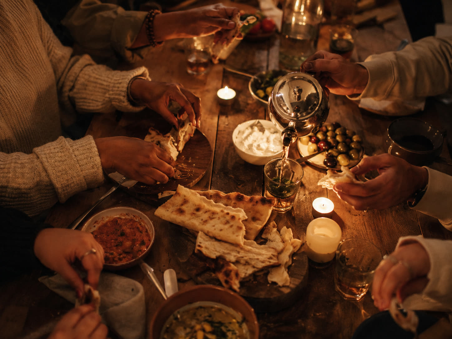 Hands sharing bread and tea at a candle-lit table